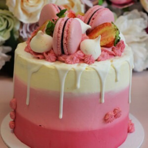 roze-lichtroze-wit-laagjes-taart-met-witte-drip-roze-macarons-aardbeien-en-meringue
