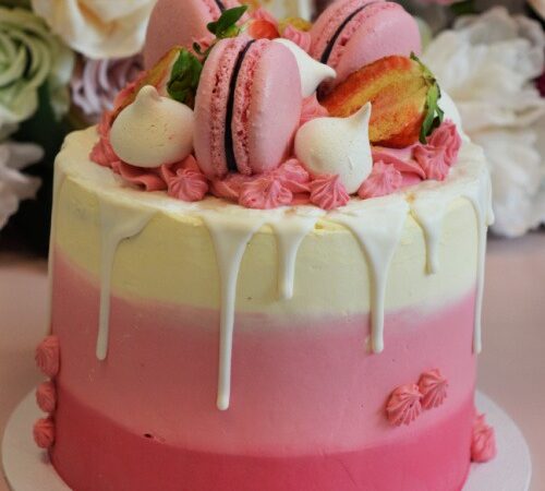 roze-lichtroze-wit-laagjes-taart-met-witte-drip-roze-macarons-aardbeien-en-meringue