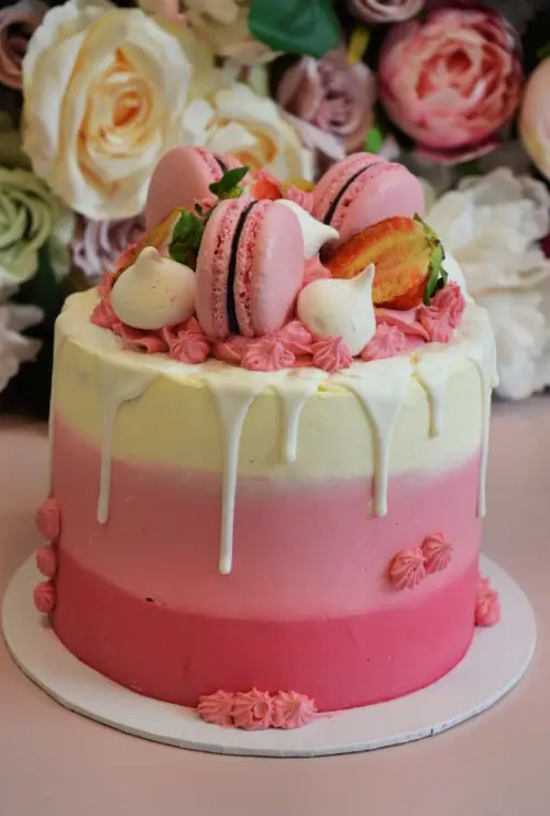 rozeombremacarontaart roze-lichtroze-wit-laagjes-taart-met-witte-drip-roze-macarons-aardbeien-en-meringue
