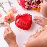A heart-shaped red cake surrounded by vibrant flowers, capturing romance and sweetness.