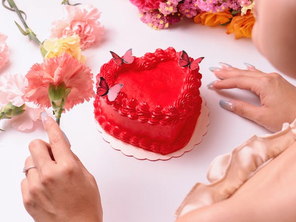 A heart-shaped red cake surrounded by vibrant flowers, capturing romance and sweetness.