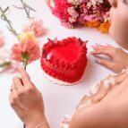 A heart-shaped red cake surrounded by vibrant flowers, capturing romance and sweetness.